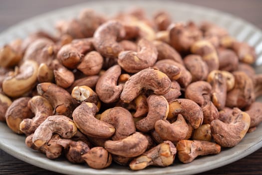 Cashew nuts with peel in a plate on wooden tray and table background, healthy raw food concept.