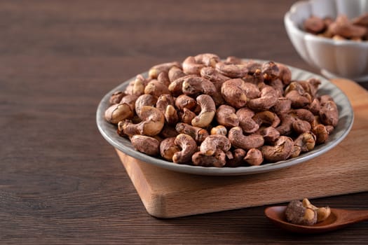 Cashew nuts with peel in a plate on wooden tray and table background, healthy raw food concept.