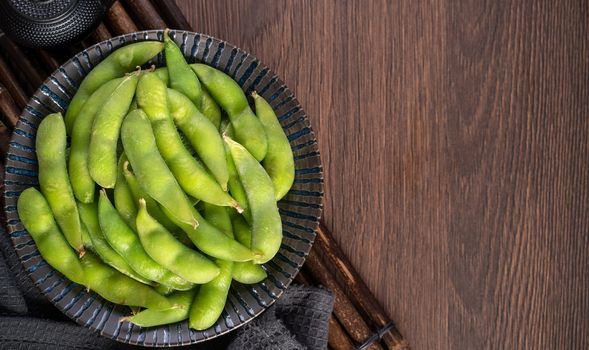 Fresh cooked boiled edamame in a plate on wooden tray and table background, healthy protein food concept.