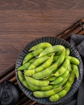 Fresh cooked boiled edamame in a plate on wooden tray and table background, healthy protein food concept.