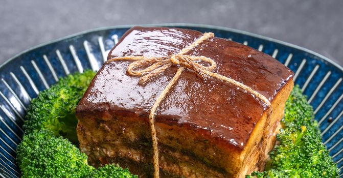 Dong Po Rou (Dongpo pork meat) in a beautiful plate with green vegetable, traditional festive food for Chinese new year cuisine meal, close up.