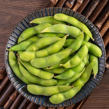 Fresh cooked boiled edamame in a plate on wooden tray and table background, healthy protein food concept.