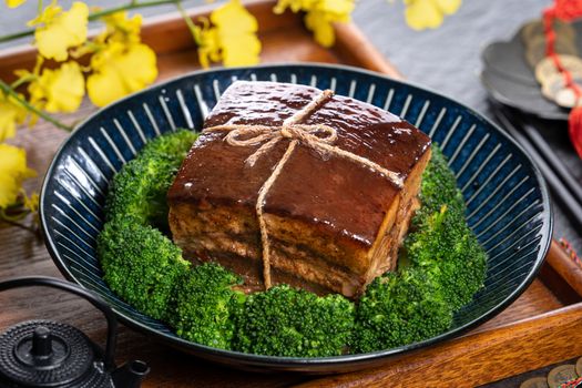 Dong Po Rou (Dongpo pork meat) in a beautiful plate with green vegetable, traditional festive food for Chinese new year cuisine meal, close up.