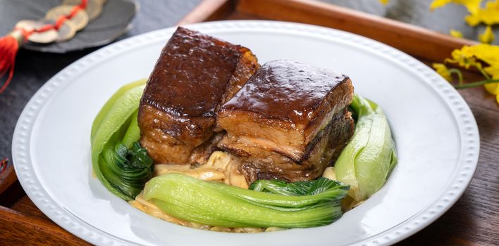 Dong Po Rou (Dongpo pork meat) in a beautiful plate with green vegetable, traditional festive food for Chinese new year cuisine meal, close up.