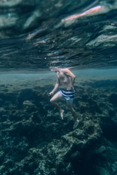 Underwater photograph of a man, boy, swimming among the rocks in the sea off the coast of Menorca.