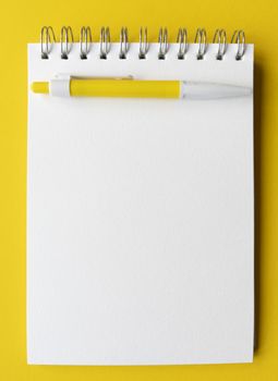 Blank sheet of notebook with pen on it. Educational concept in yellow and white colors. Stock photo.