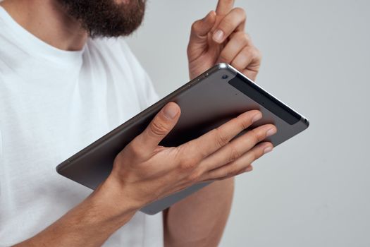 Tablet with a touch screen on a light background male hands white t-shirt cropped view. High quality photo