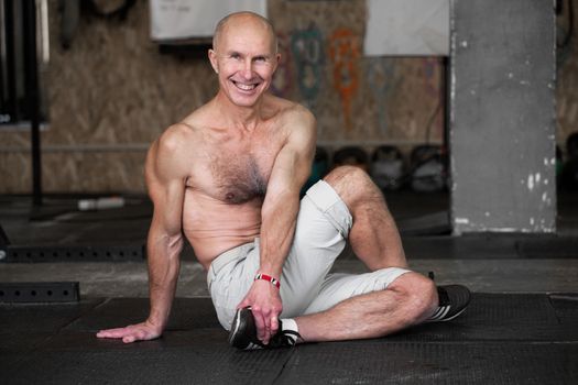 Happy smiling muscular athletic senior man doing yoga exercise in gym