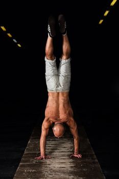 Senior man standing on hands upside down in dark gym