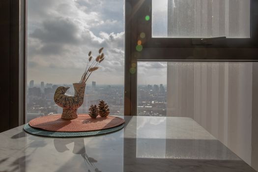 Dried flowers in beautiful ceramic blue vase handmade with two pine cones on table of living room and city view. Home decor. Space for text. Selective focus.