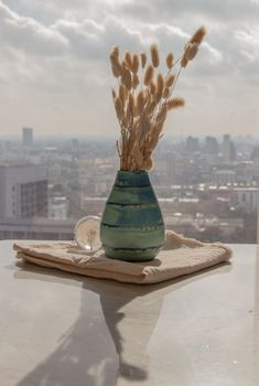 Dried flowers in beautiful ceramic blue vase handmade with glass paper weight on marble table of living room and city view. Home decor. Space for text. Selective focus.