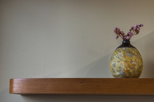 Dried flowers in beautiful ceramic yellow vase standing on wooden shelf on wall of living room. Home decor. Space for text. Selective focus.