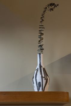 Dried flowers in beautiful ceramic black and white vase standing on wooden shelf on wall of living room. Home decor. Space for text. Selective focus.