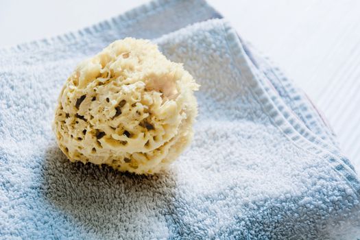 A natural yellow sponge on towels stacked on a white wooden table. Personal care and hygiene. Bath and relax