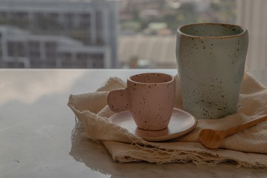 Blue and pink ceramics mugs handmade with wooden spoon on marble table of living room and city view. Home decor. Space for text. No focus, specifically.