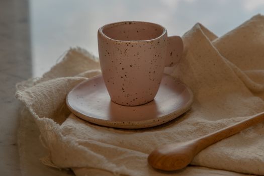 Pink ceramic mug handmade with wooden spoon on marble table of living room and city view. Home decor. Space for text.