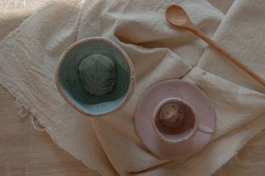 Blue and pink ceramics mugs handmade with wooden spoon on white calico. Home decor. Space for text. No focus, specifically.