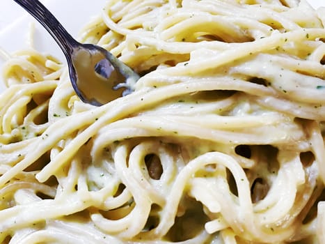 A fork in a plate of creamy spaghetti. Italian food. Carbohydrates and recipes with cream