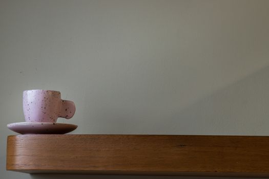 Pink ceramic mug handmade on the wooden shelf on wall of living room. Home decor. Space for text. Selective focus.