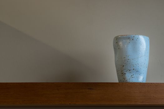 Blue ceramic mug handmade on the wooden shelf on wall of living room. Home decor. Space for text. Selective focus.