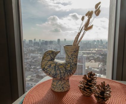 Dried flowers in beautiful ceramic blue vase handmade with two pine cones on table of living room and city view. Home decor. Space for text. Selective focus.