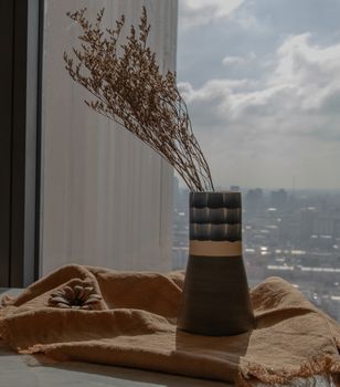 Dried flowers in beautiful ceramic blue vase handmade on table of living room and city view. Home decor. Space for text. Selective focus.