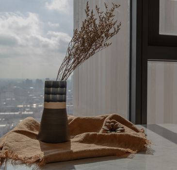 Dried flowers in beautiful ceramic blue vase handmade on table of living room and city view. Home decor. Space for text. Selective focus.