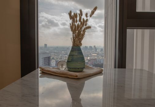 Dried flowers in beautiful ceramic blue vase handmade with glass paper weight on marble table of living room and city view. Home decor. Space for text. Selective focus.