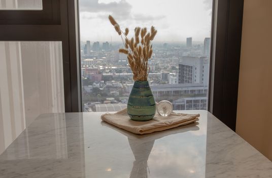 Dried flowers in beautiful ceramic blue vase handmade with glass paper weight on marble table of living room and city view. Home decor. Space for text. Selective focus.