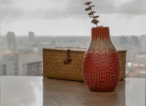 Dried flowers in beautiful ceramic red vase handmade with Woven rattan traditional box on marble table of living room and city view. Home decor. Space for text. Selective focus.