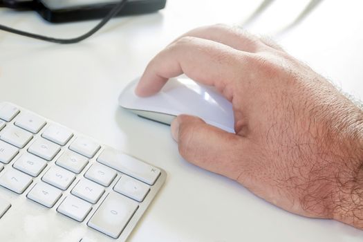 the white hand of a caucasian man working on a computer clicking a white mouse near a computer keyboard. Place of work and office. Wireless technology