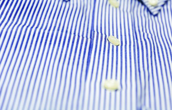 The button of a blue striped shirt with a button down collar. Formal wear for events or work and business meetings
