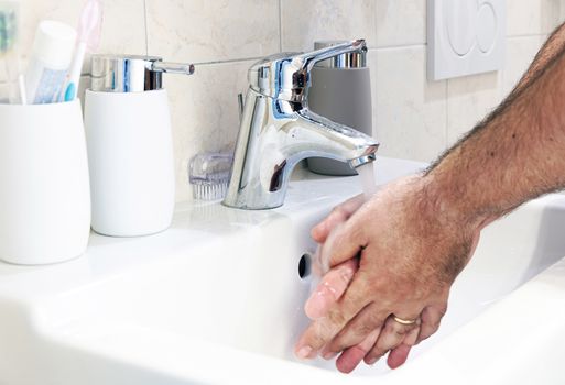 a man washing his hands in a white ceramic sink. Personal care and cleaning. Chrome tap and soap container