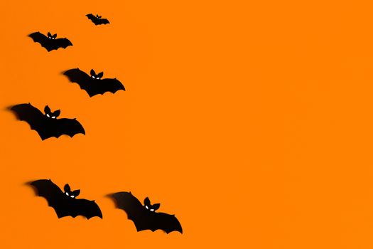 orange background with a flock of black paper bats for Halloween, black paper bat silhouettes on an orange background, Halloween concept, copyspace, flatlay, top view, overhead.