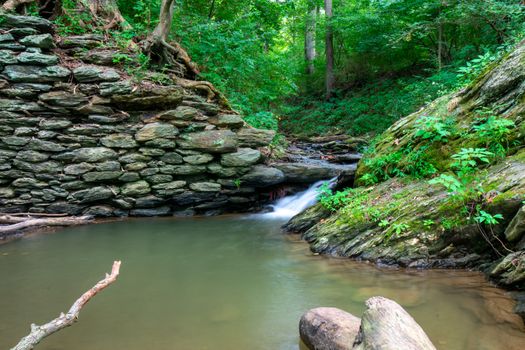 A Long Exposure of a Stream of Water Flowing Into a Small Body of Water Next to a Cobblestone Wall