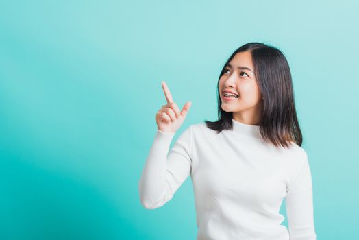 Portrait of Asian teen beautiful young woman smile have dental braces on teeth laughing point finger side away blank copy space, studio shot isolated on blue background, medicine and dentistry concept