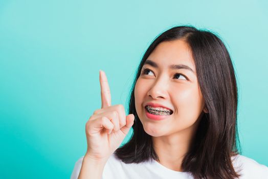 Portrait of Asian teen beautiful young woman smile have dental braces on teeth laughing point finger side away blank copy space, studio shot isolated on blue background, medicine and dentistry concept