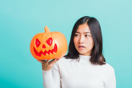 Portrait of Asian beautiful young woman holding orange model pumpkins, funny happy female with ghost pumpkins, studio shot isolated on blue background