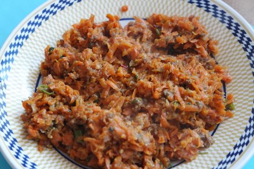 Top closeup view of a homemade dish made from carrot and vegetables served in a ceramic plate.