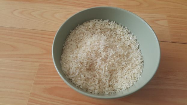 Top closeup view of heap of rice in a ceramic bowl placed over wooden floor.