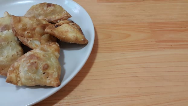 Closeup of delicious home made spicy and crunchy samosa pastries placed in a white ceramic plate on wooden floor