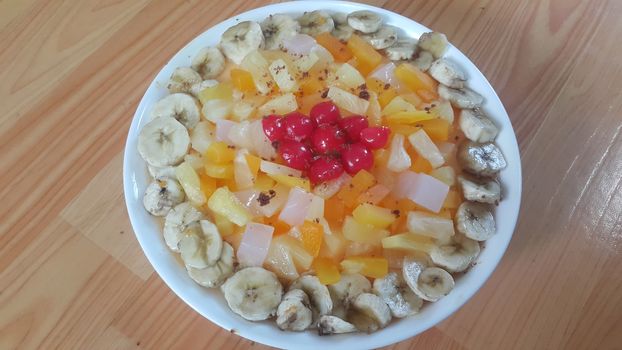 Creamy tasty sweet fruit trifle over custard with banana slices layered on surface on wooden floor. A top view of home made fruit trifle, a products for dessert after meal.