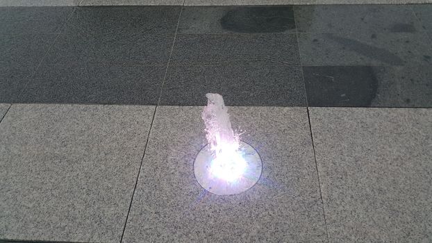 Beautiful and colorful light water fountain over concrete floor. Colorful water shape on fountain with grey background.