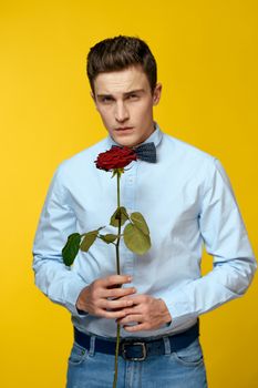 Gentleman in shirt and bow tie around his neck yellow background red rose. High quality photo