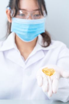 Close up Scientist hands putting in nitrile latex gloves holding Omega 3 capsule in labcoat wearing nitrile gloves, doing experiments in lab