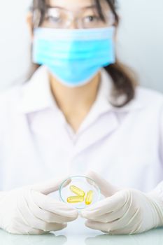 Close up Scientist hands putting in nitrile latex gloves holding Omega 3 capsule in labcoat doing experiments in lab