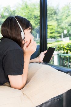 Young girl with headphones and listening to music from mobile phone on the sofa in living room at home