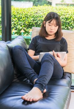 Young girl studying online from digital tablet on the sofai n living room at home