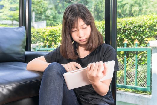 Young girl studying online from digital tablet on the sofai n living room at home