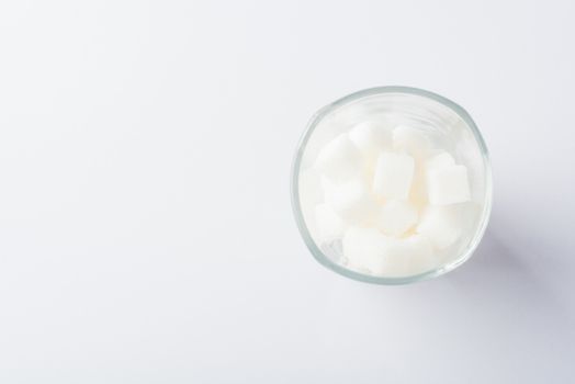 Top view glass full of white sugar cube sweet food ingredient, studio shot isolated on white background, health high blood risk of diabetes and calorie intake concept and unhealthy drink